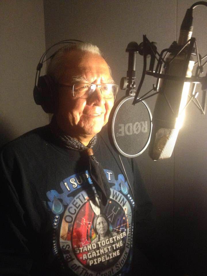 Elder Gerry Oleman wearing headphones beside a studio microphone and pop filter at UBC Studios in 2017.
