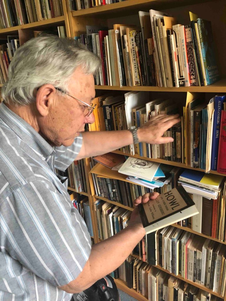 Robert Hogg holds a copy of Howl while showing Craig Carpenter the poetry books in his attic writing room.
