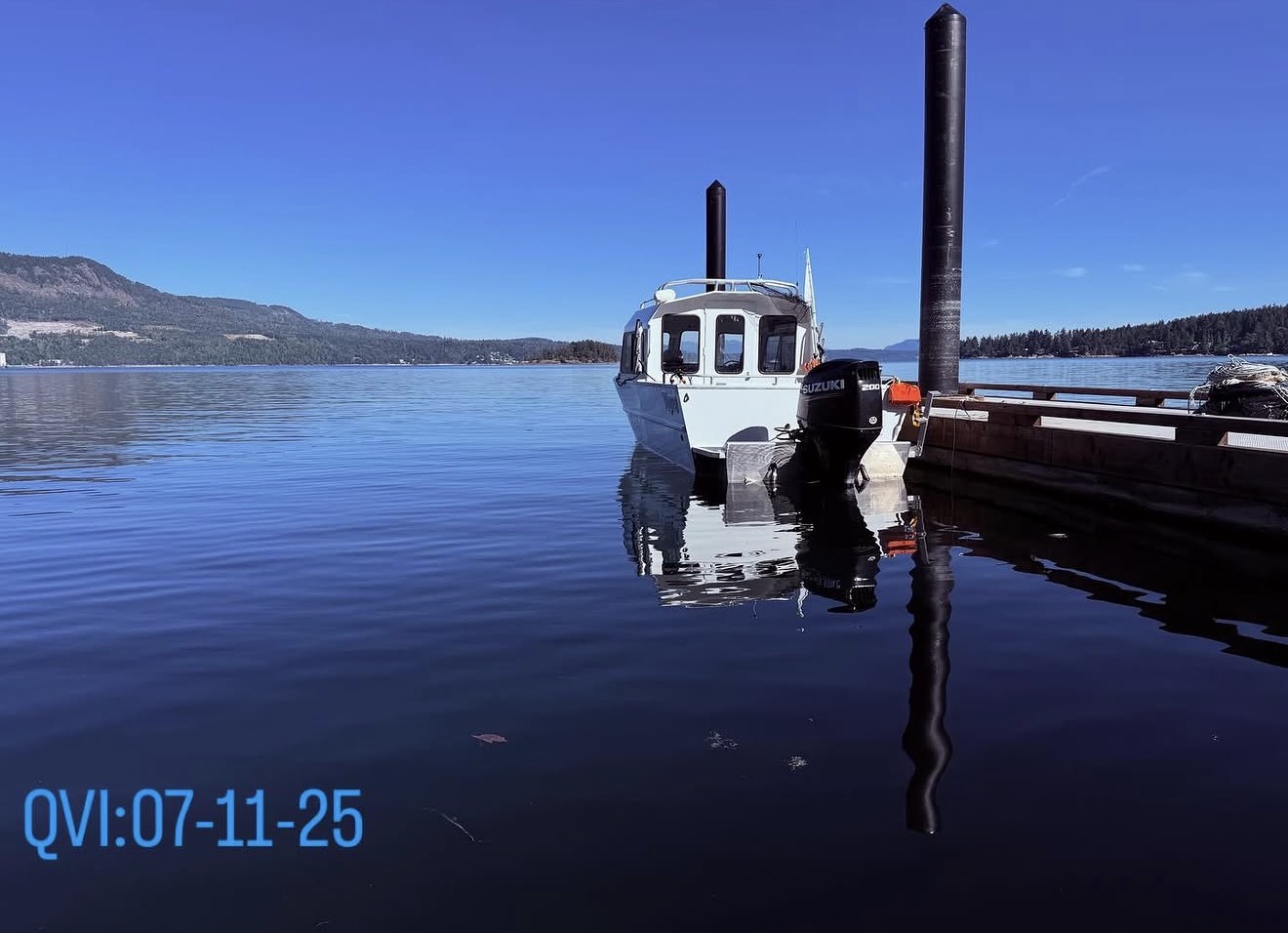 Boat used by the Guardians moored beside a dock on Saanich Inlet, with forested hills across the water.